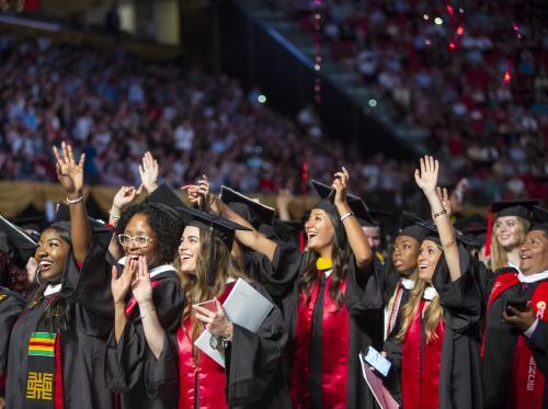 Students in graduation regalia waving during the University commencement ceremony.